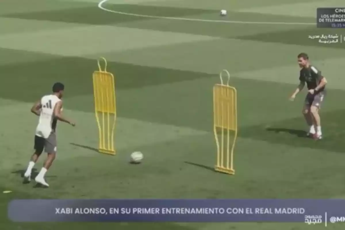 Dos futbolistas entrenan en un campo de fútbol con maniquíes amarillos y un balón mientras el sol brilla y el césped está bien cuidado Dos futbolistas entrenan en un campo de fútbol con maniquíes amarillos y un balón mientras el sol brilla y el césped está bien cuidado