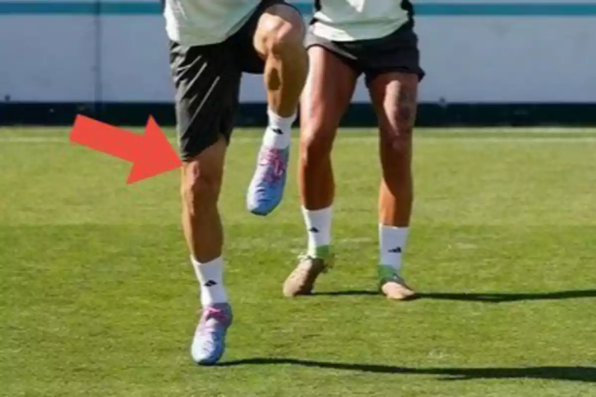 Dos personas entrenando en un campo de fútbol mientras una flecha roja señala la pierna de uno de ellos Dos personas entrenando en un campo de fútbol mientras una flecha roja señala la pierna de uno de ellos