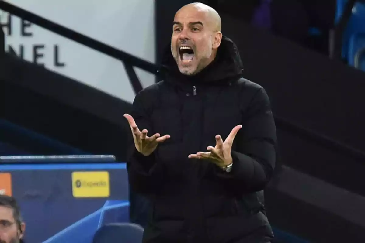 A bald man with a beard is gesturing energetically while wearing a black jacket in a sports environment. A bald man with a beard is gesturing energetically while wearing a black jacket in a sports environment.