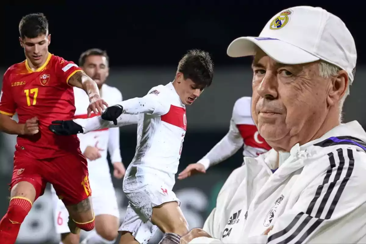 Un entrenador de fútbol con gorra blanca observa un partido en el que un jugador de rojo compite con uno de blanco.