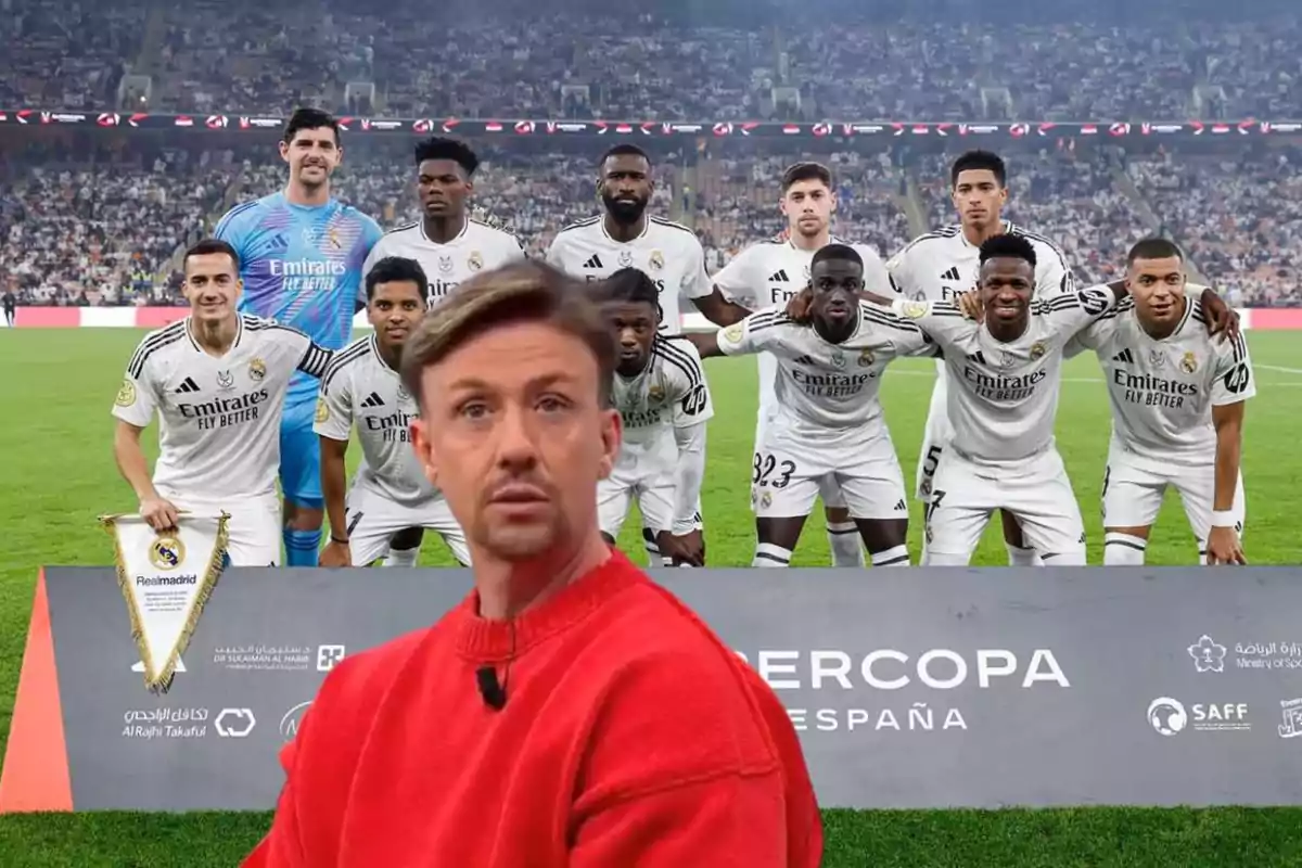 A soccer team posing on the field with a man in the foreground wearing a red sweater.