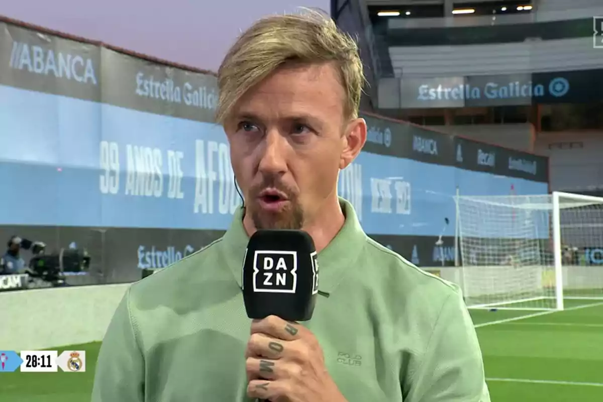 A man with a DAZN microphone at a soccer stadium. A man with a DAZN microphone at a soccer stadium.