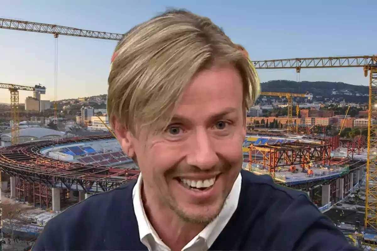 Un hombre sonriente con cabello rubio frente a un estadio en construcción con grúas en el fondo.