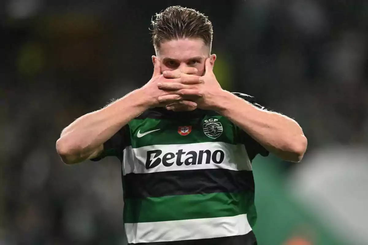 A football player who wears a sporty Lisbon jersey covers his mouth with his hands on the field.