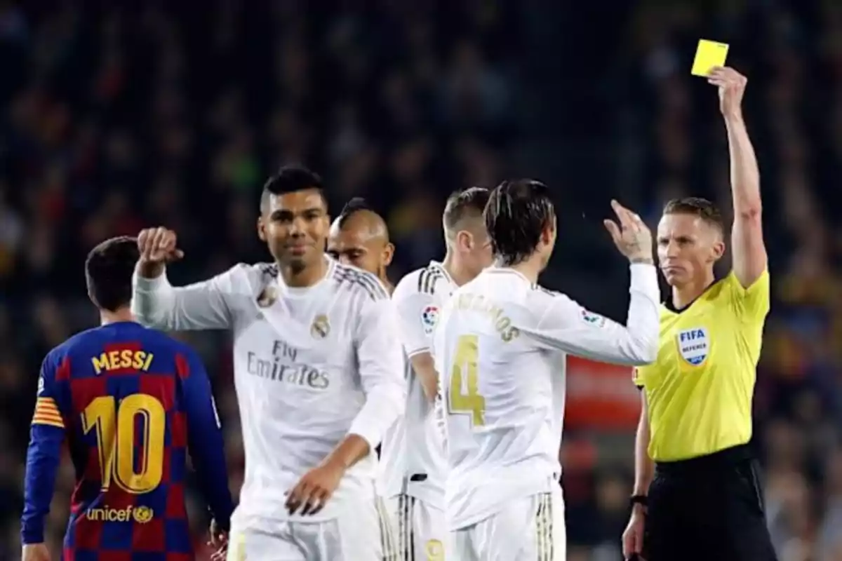 A referee shows a yellow card to a player during a soccer match between two teams with white and blue and red uniforms. A referee shows a yellow card to a player during a soccer match between two teams with white and blue and red uniforms.