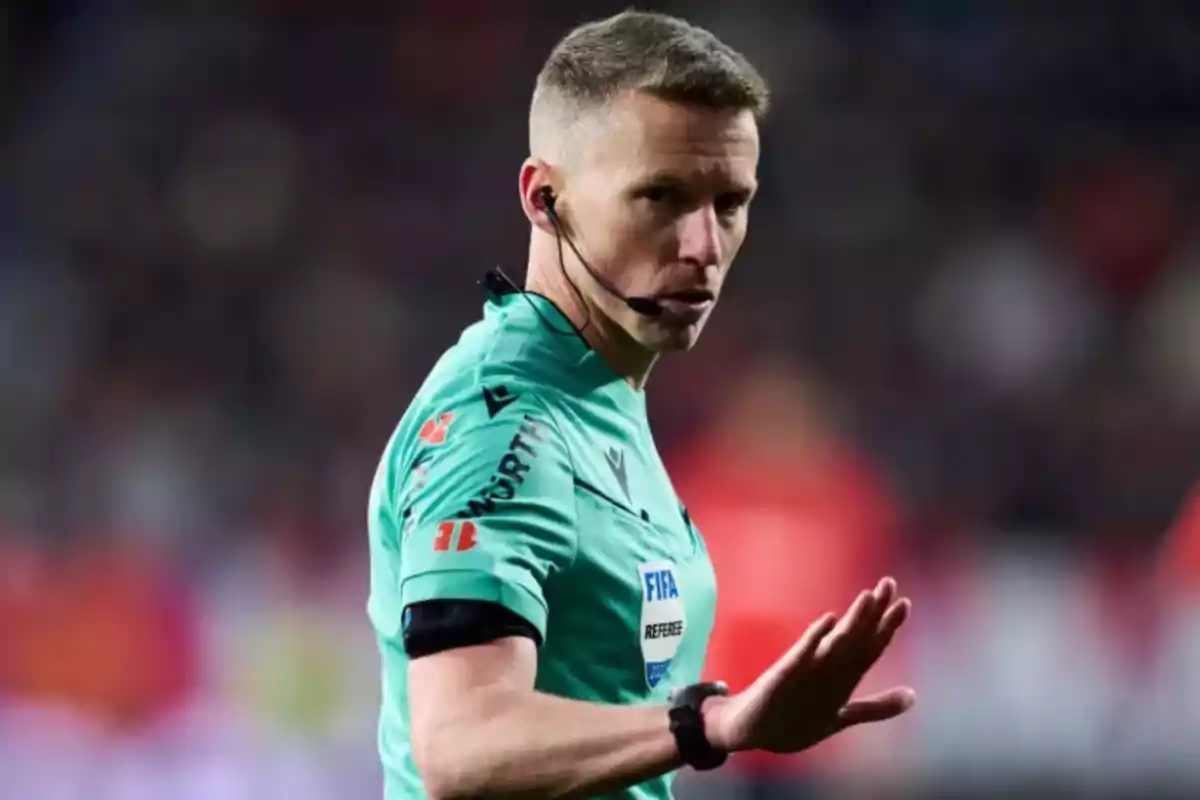A soccer referee in a green uniform and earpiece gestures with his hand in a stadium. A soccer referee in a green uniform and earpiece gestures with his hand in a stadium.