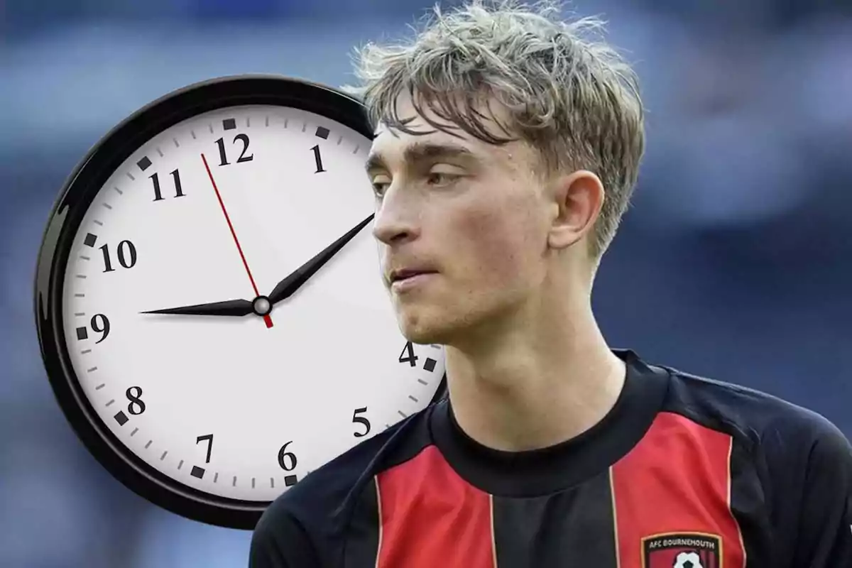 Un jugador de fútbol con una camiseta roja y negra está frente a un reloj grande que marca las 11:10.