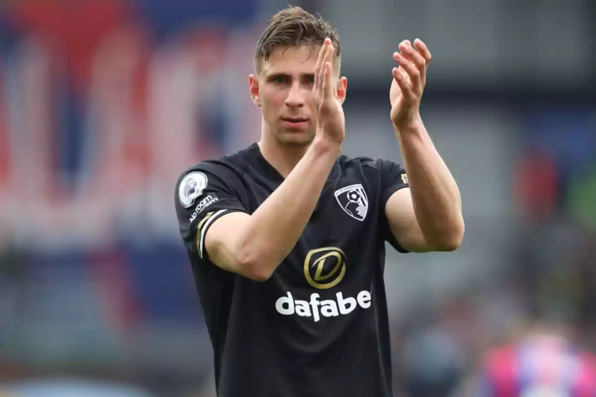 A soccer player applauding on the field in a black jersey.