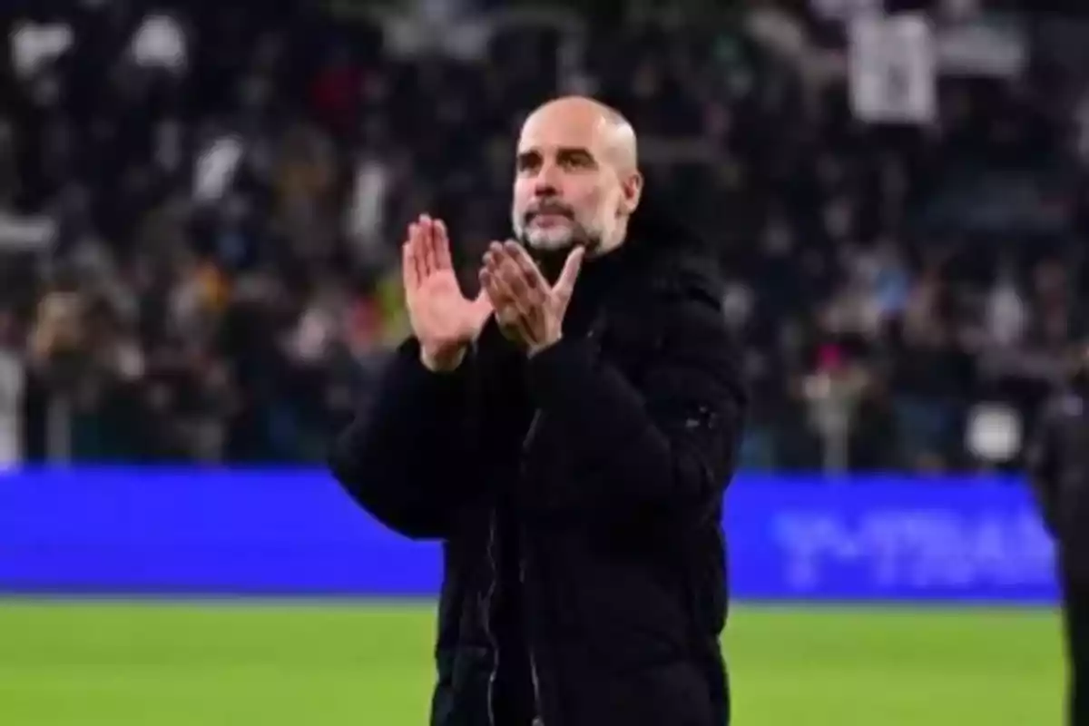 A man clapping in a stadium wearing a black coat.