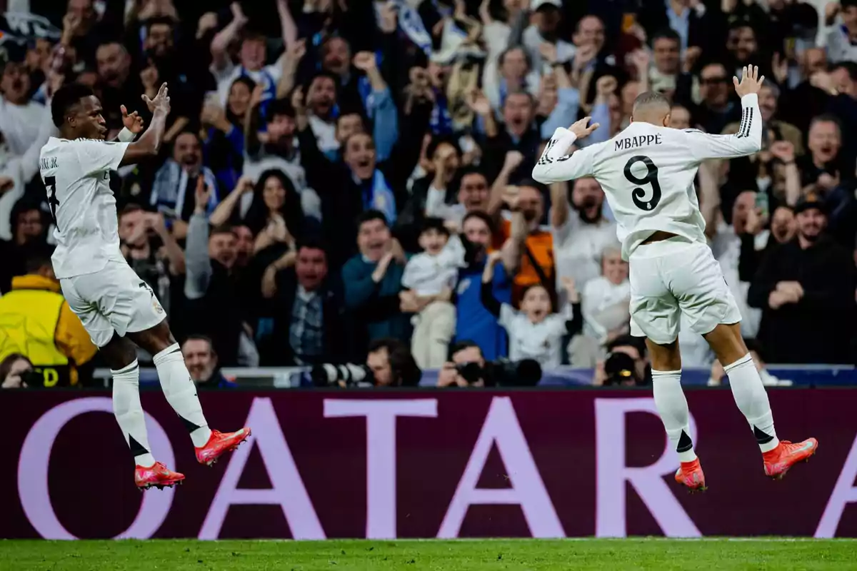 Two players celebrate a goal in front of a crowd of excited fans in a stadium.