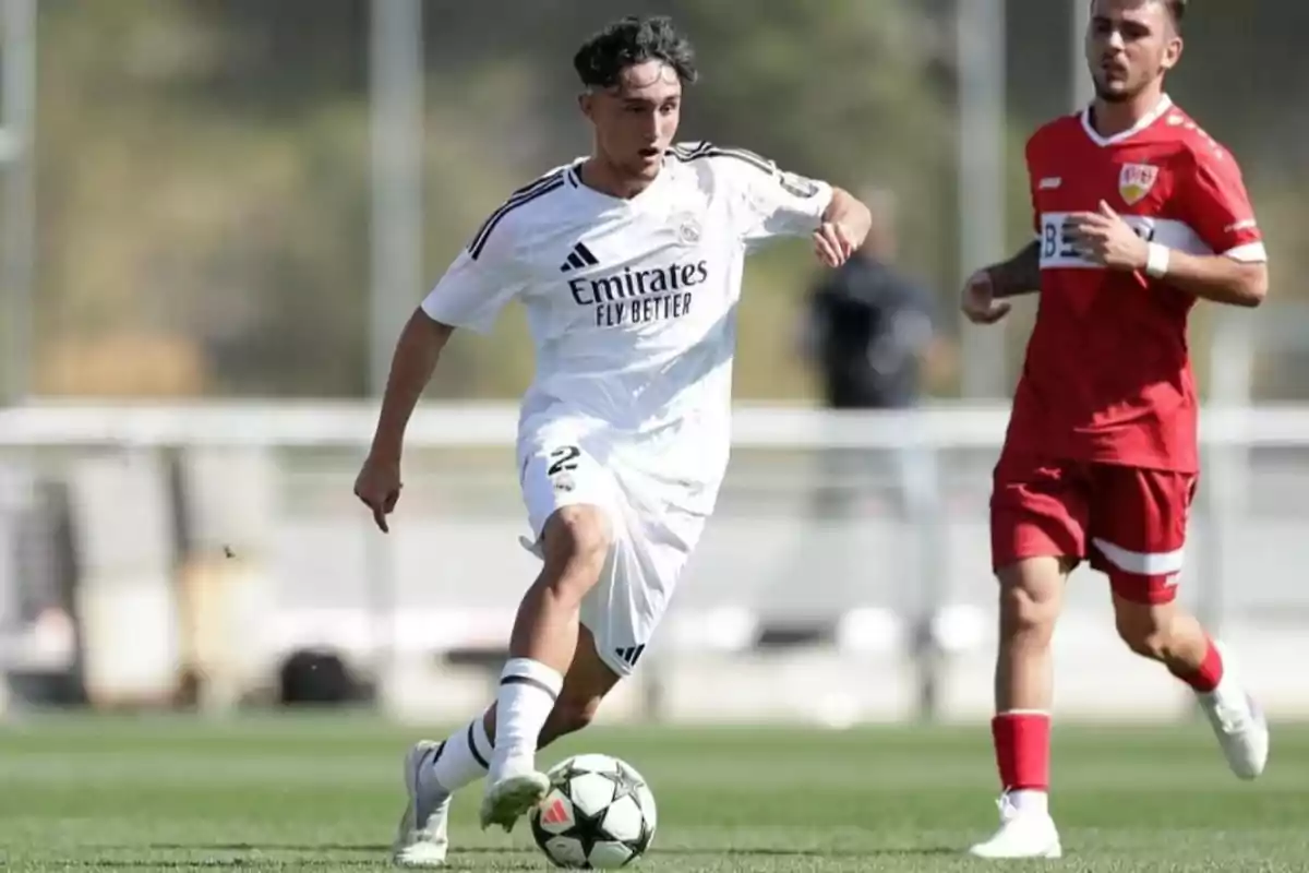 Soccer player in a white uniform controls the ball while an opponent in a red uniform follows him during an outdoor match. Soccer player in a white uniform controls the ball while an opponent in a red uniform follows him during an outdoor match.
