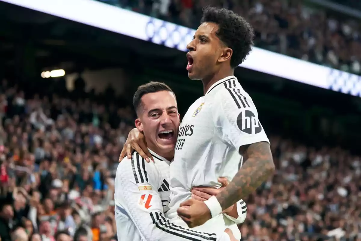 Dos jugadores de fútbol celebrando un gol en un estadio lleno de espectadores.