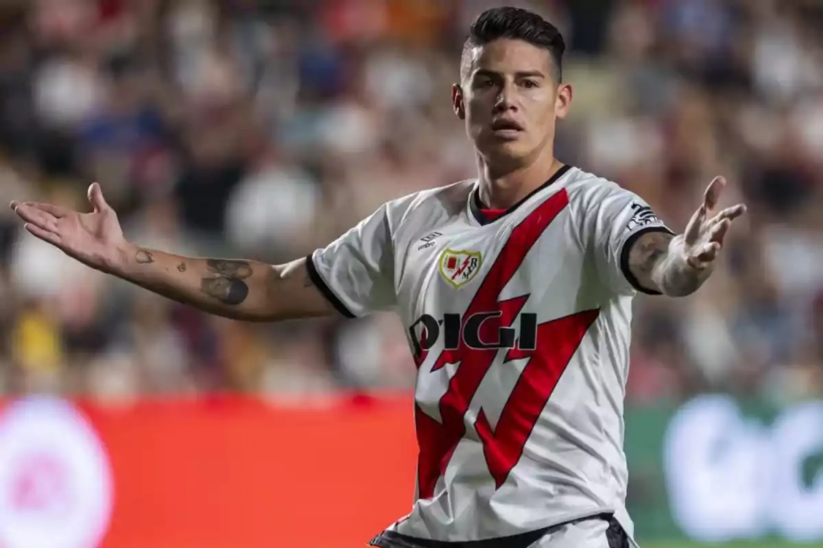 Un jugador de fútbol con uniforme blanco y rojo gesticula con los brazos abiertos en un estadio.