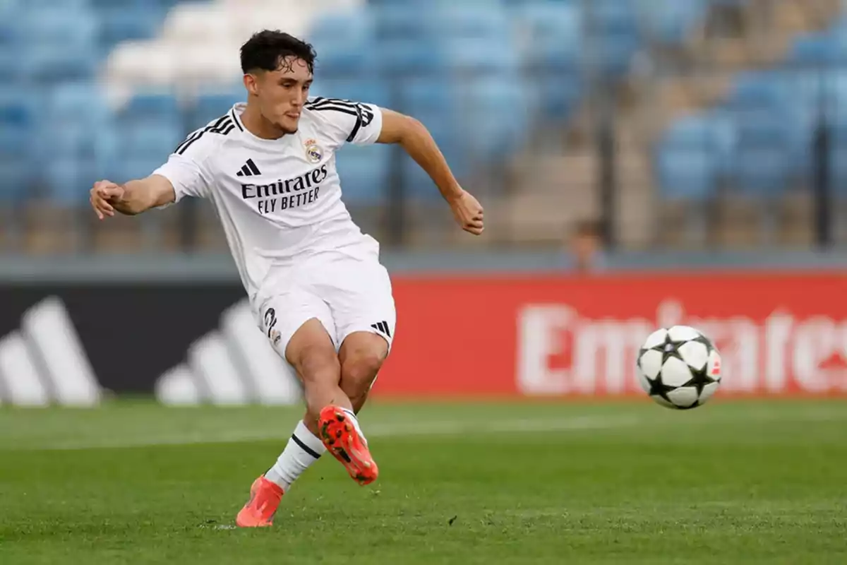 Jugador de fútbol del Real Madrid con uniforme blanco pateando un balón en un estadio