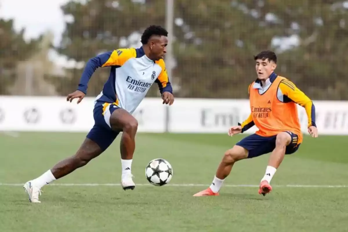 Two players are training on a soccer field; one is wearing an orange bib and the other is controlling the ball with his left leg. Two players are training on a soccer field; one is wearing an orange bib and the other is controlling the ball with his left leg.