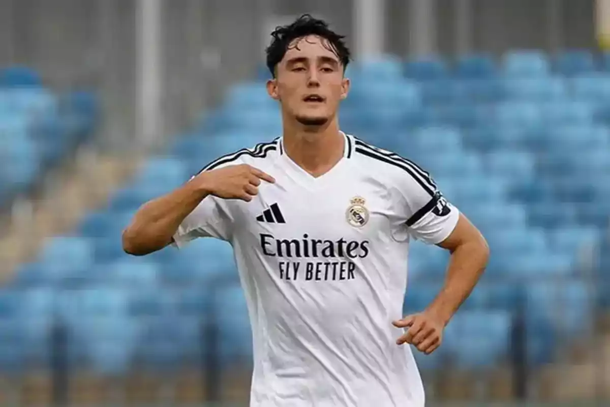 Jugador de fútbol con uniforme blanco del Real Madrid celebrando en un estadio con gradas azules de fondo
