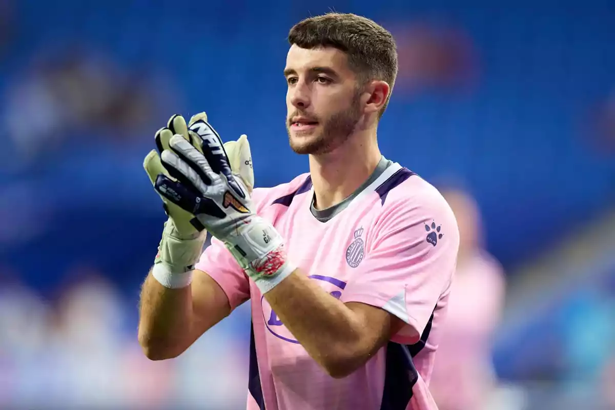 A player in a pink uniform and goalkeeper gloves claps in a stadium. A player in a pink uniform and goalkeeper gloves claps in a stadium.