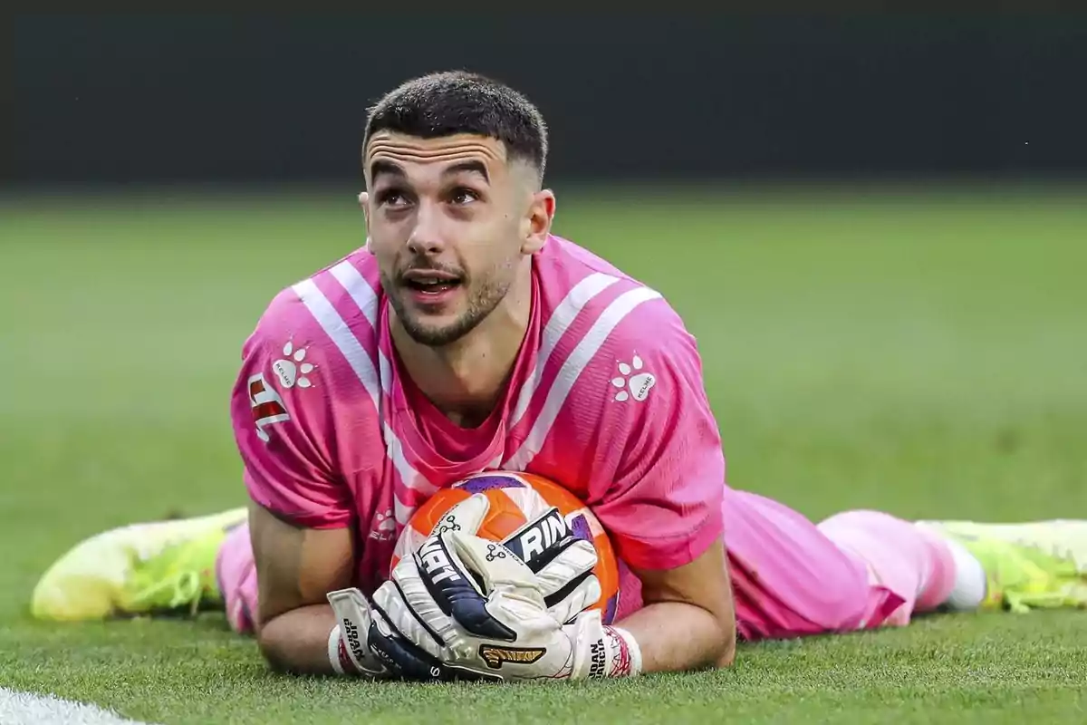 Goalkeeper in a pink uniform lying on the grass holding a soccer ball Goalkeeper in a pink uniform lying on the grass holding a soccer ball