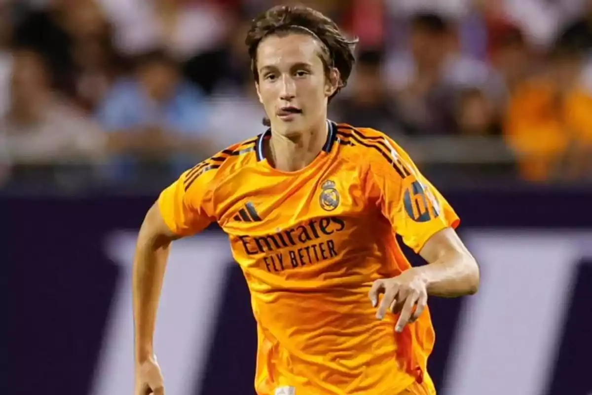 A player in an orange Real Madrid uniform runs on the field during a match. A player in an orange Real Madrid uniform runs on the field during a match.