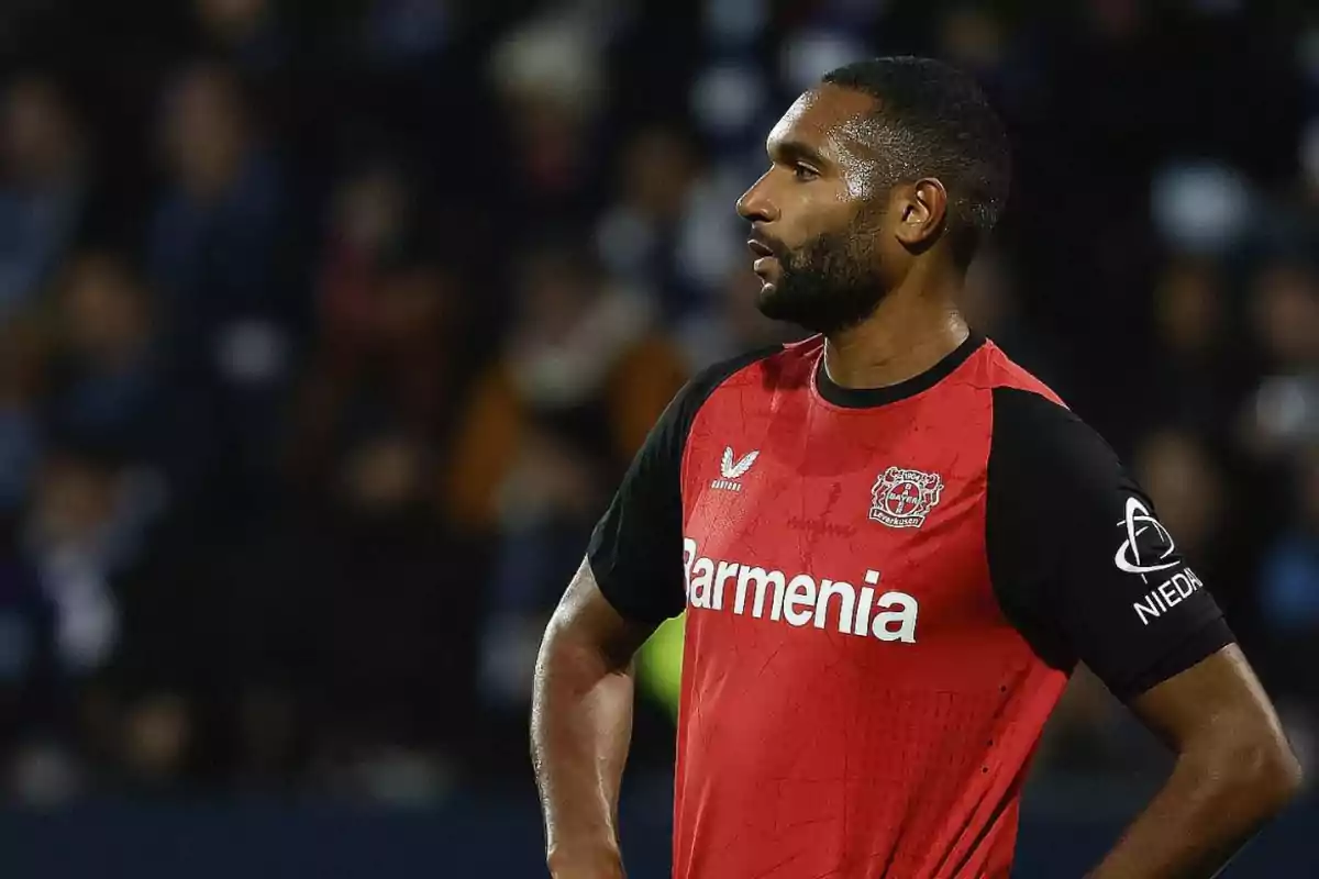 Un jugador de fútbol con uniforme rojo y negro del Bayer Leverkusen está en el campo durante un partido.