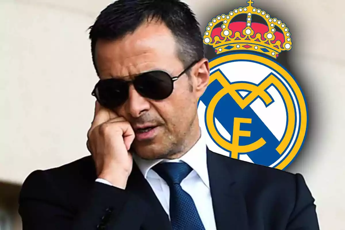 Man wearing sunglasses and a suit talking on the phone with the Real Madrid crest in the background