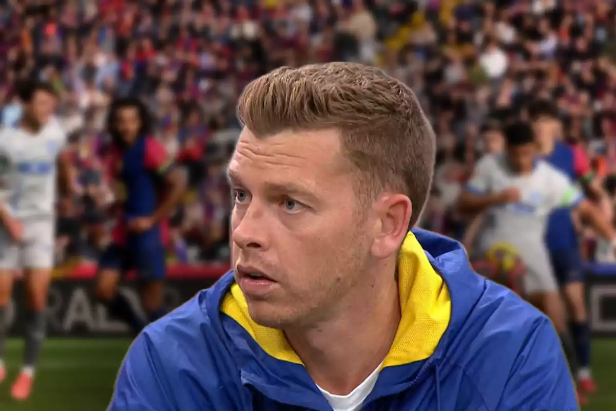 A man in a blue jacket with a yellow hood is in the foreground, while in the background a soccer match with blurred players and spectators can be seen.