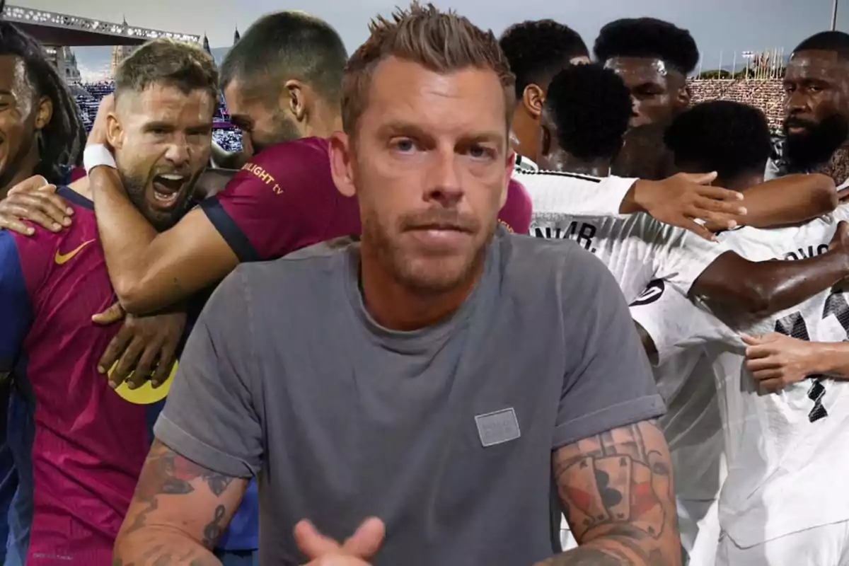 A man with tattoos on his arms is sitting in front of the camera while behind him two groups of players are hugging, one wearing blue and maroon jerseys and the other wearing white jerseys.