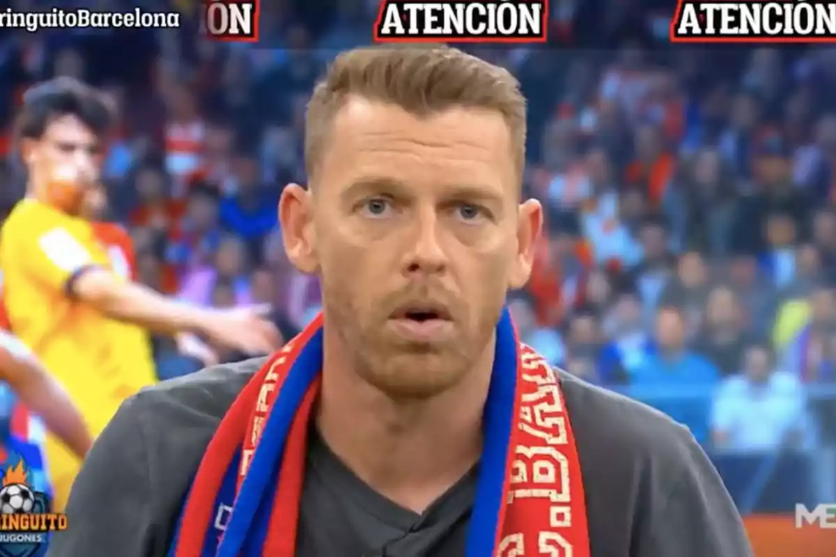 A man with a red and blue scarf is in a television studio with a blurred background of a soccer match.