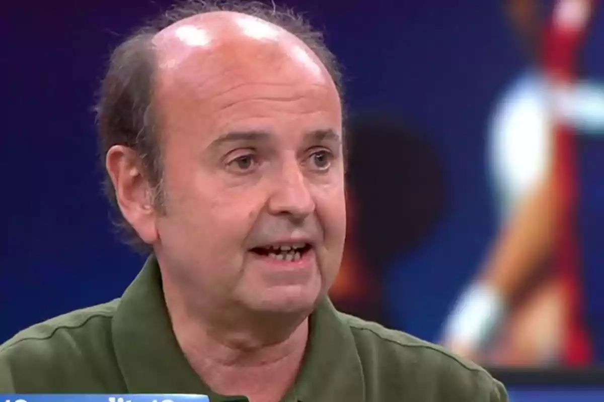 Un hombre calvo con camisa verde hablando en un programa de televisión con un fondo desenfocado.