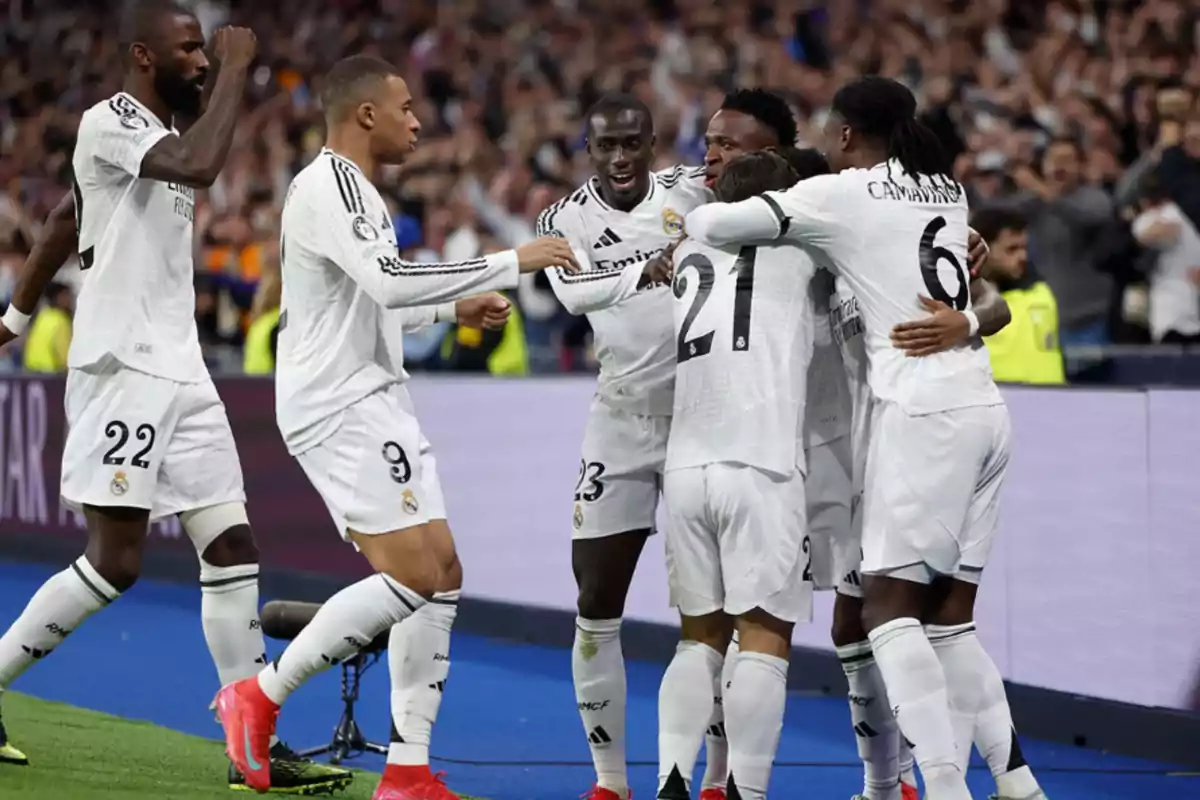 Soccer players celebrating a goal on the field in white uniforms.