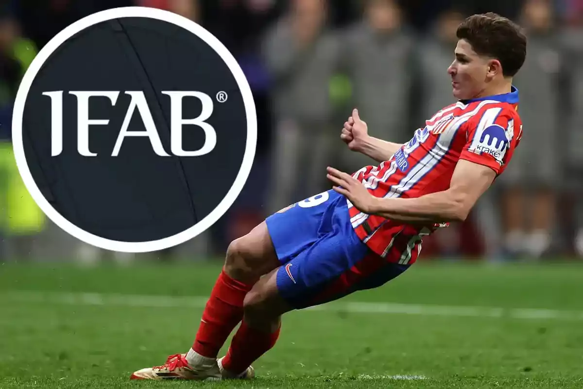Soccer player in a red and white uniform sliding on the field next to the IFAB logo in the foreground