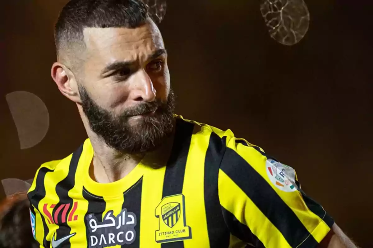 A soccer player with a beard and short hair wears a yellow and black Al-Ittihad club jersey.