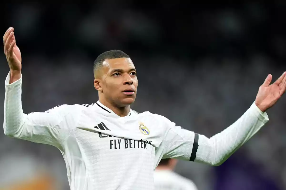 Un jugador de fútbol con uniforme blanco levanta los brazos en el campo.