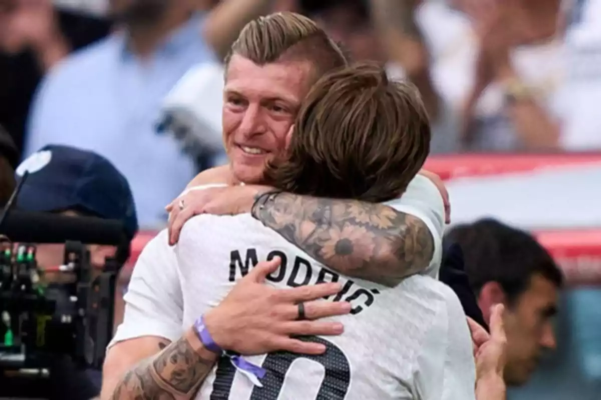 Two players hug on the field while celebrating; one of them is wearing a jersey with the name Modric. Two players hug on the field while celebrating; one of them is wearing a jersey with the name Modric.