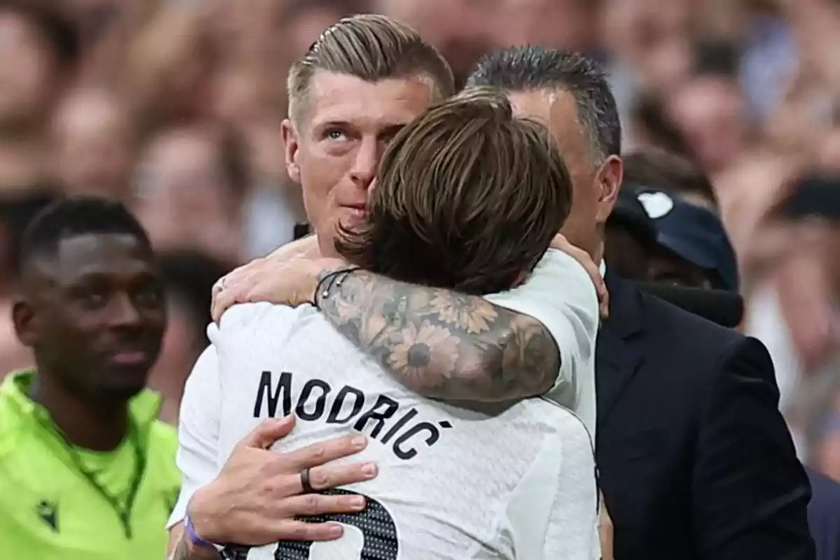 Two players hug each other excitedly on the field during an important match while a crowd watches in the background. Two players hug each other excitedly on the field during an important match while a crowd watches in the background.