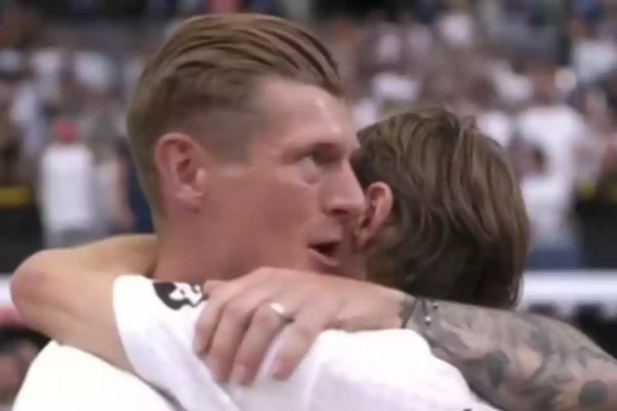 Two people hug in a sports setting full of spectators.