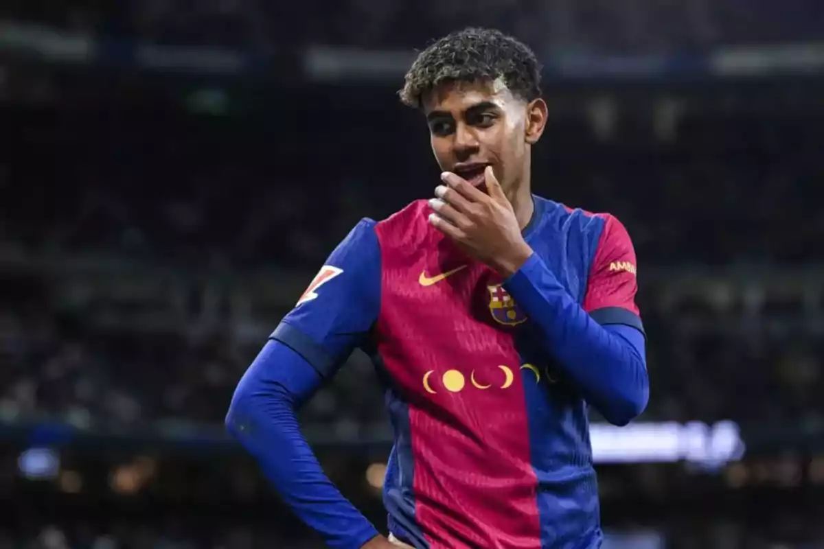 Futbolista con uniforme azul y rojo del Barcelona en el campo durante un partido, con la mano en la boca y expresión pensativa.