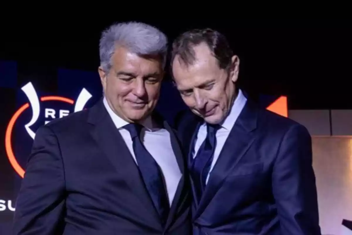 Two men dressed in dark suits hug each other at a formal event. Two men dressed in dark suits hug each other at a formal event.