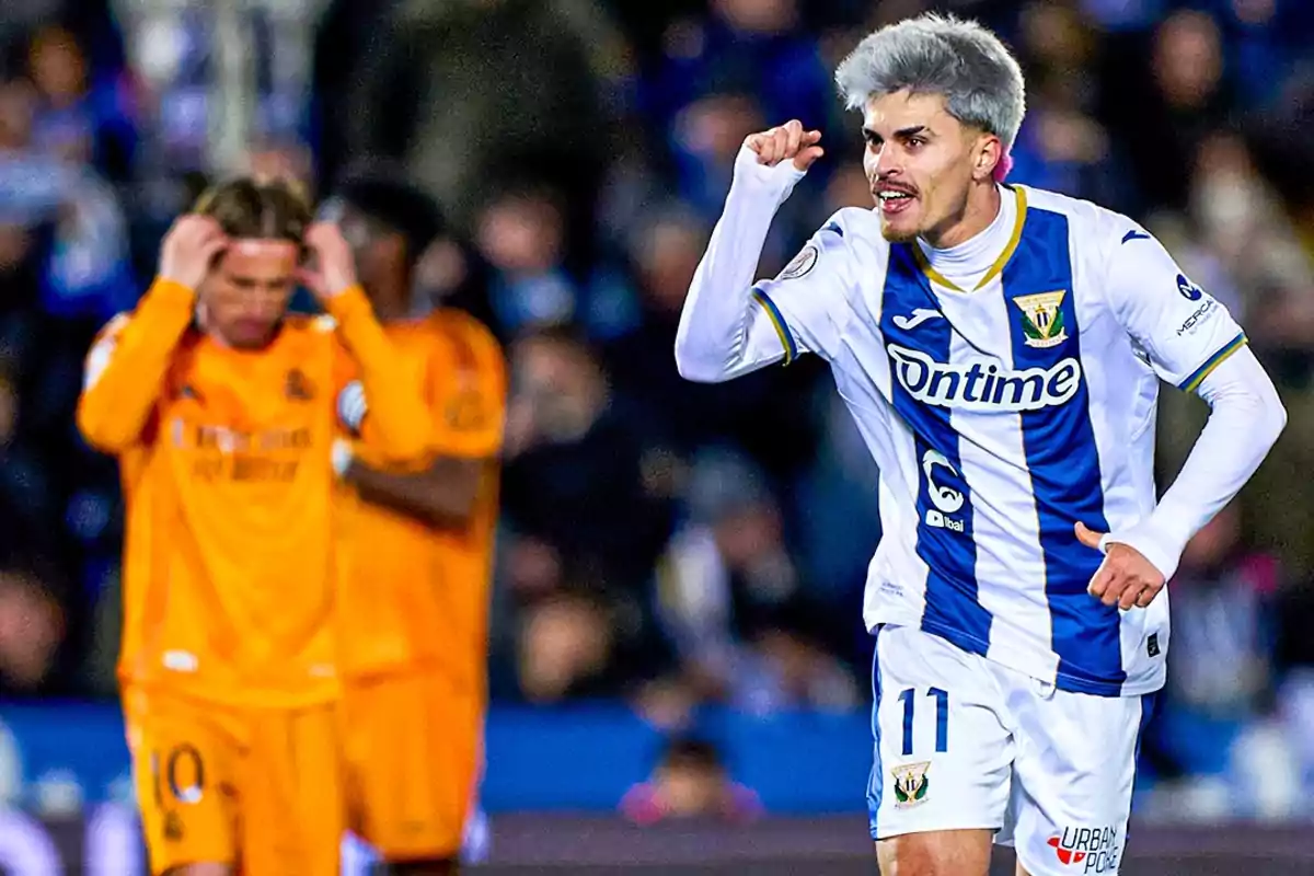 Soccer player celebrating a goal while another player in the background looks disappointed.