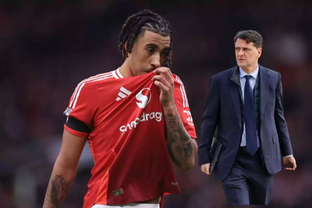 A player in a red jersey covers his mouth while a man in a suit walks behind him.