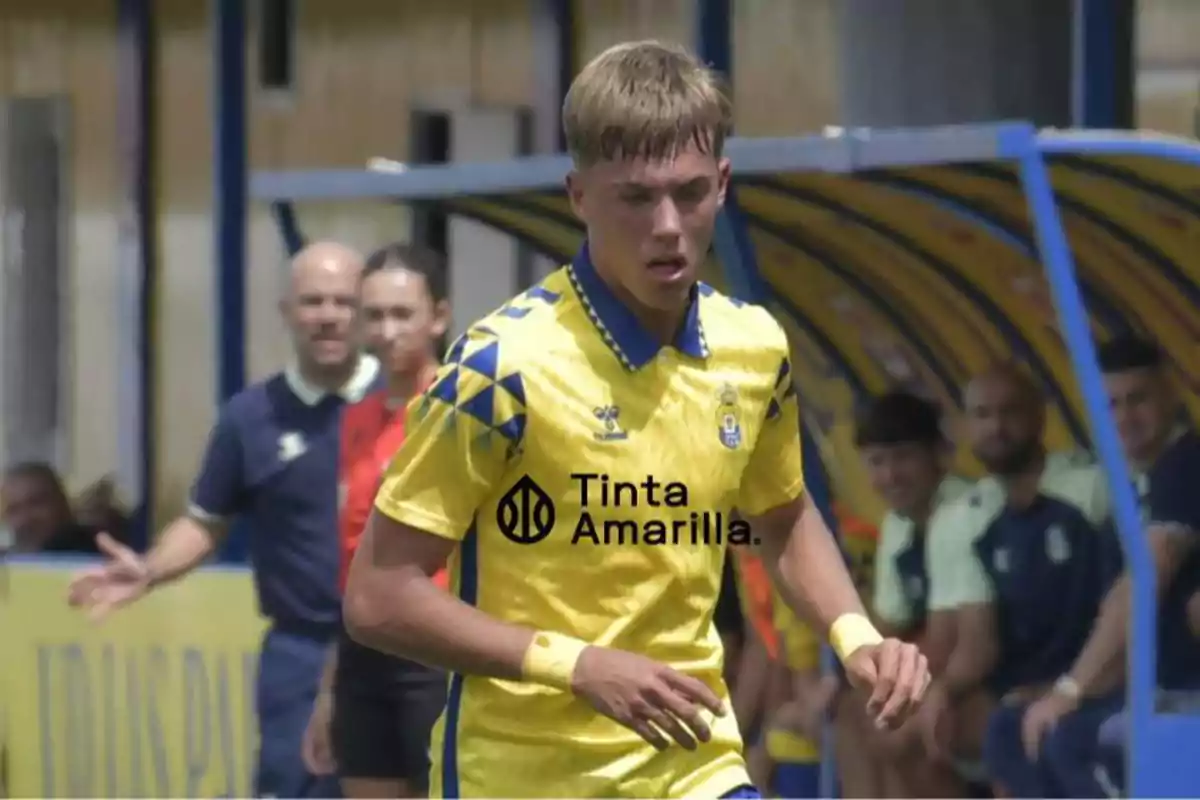 A player in a yellow uniform runs on the field while people watch from the bench.