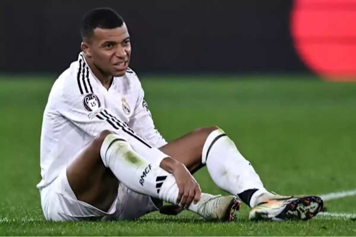 Un jugador de fútbol con uniforme blanco sentado en el campo de juego.