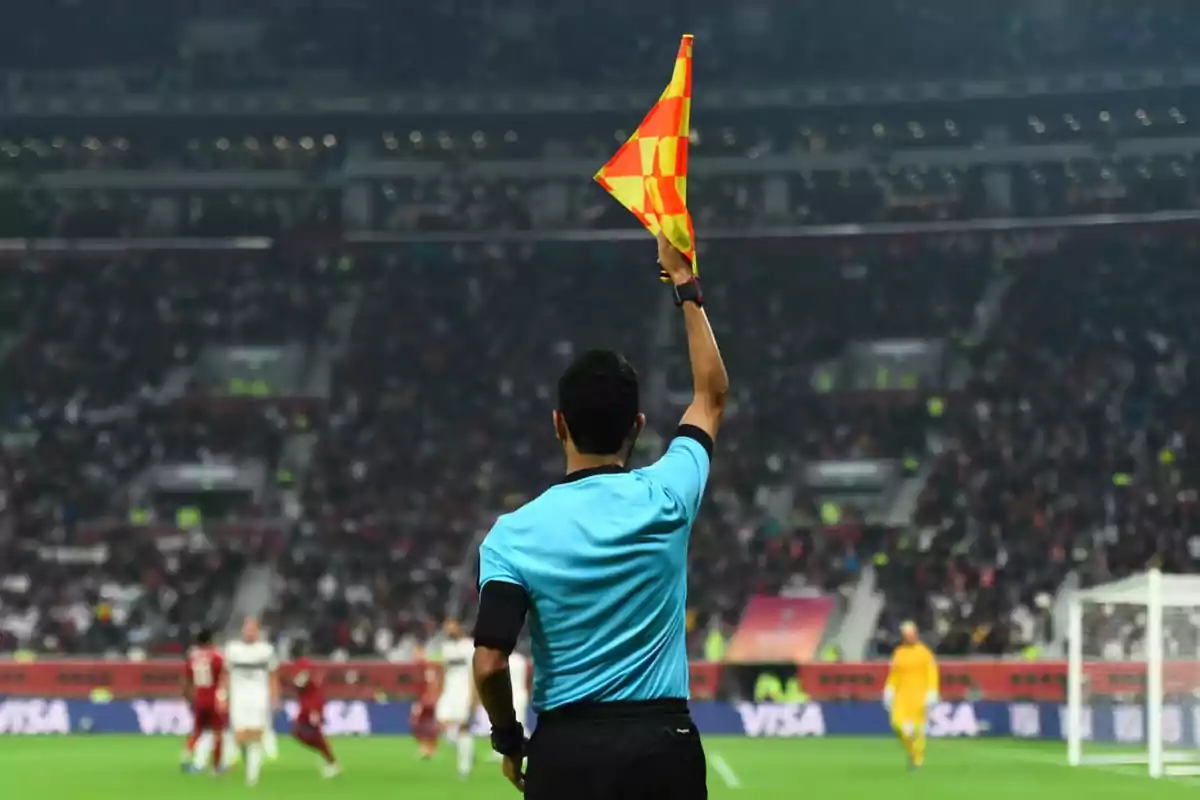 A soccer assistant referee raises their flag in a stadium full of spectators.