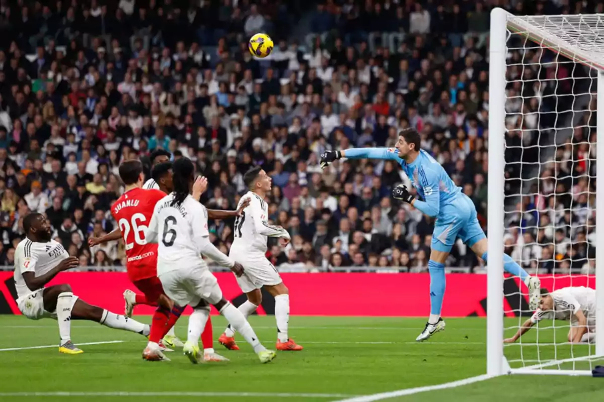 Soccer players in action during a match, with the goalkeeper jumping to try to stop the ball near the goal. Soccer players in action during a match, with the goalkeeper jumping to try to stop the ball near the goal.