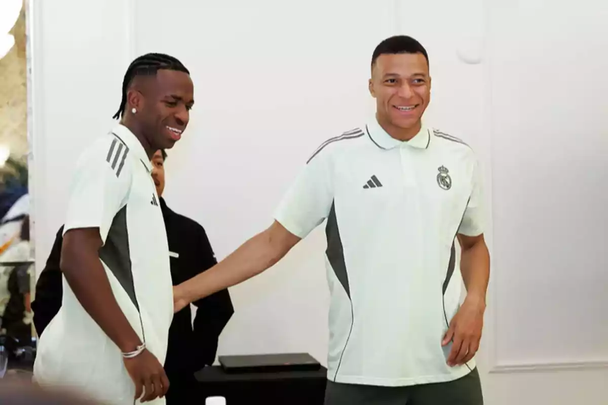 Two players in Real Madrid training uniforms smile and greet each other in a white room. Two players in Real Madrid training uniforms smile and greet each other in a white room.