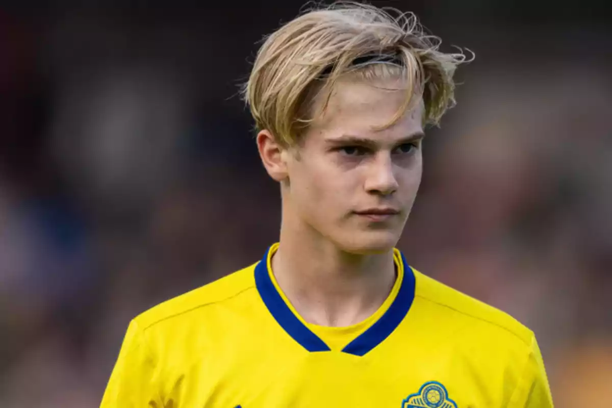 A young man in a yellow soccer jersey with slicked-back blonde hair. A young man in a yellow soccer jersey with slicked-back blonde hair.