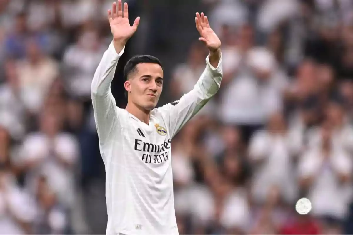 A player in a white uniform raises his hands in greeting in a stadium full of spectators.