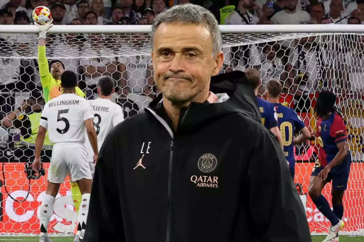 Un entrenador de fútbol con expresión seria está de pie frente a un partido en el que un portero hace una parada mientras varios jugadores observan.