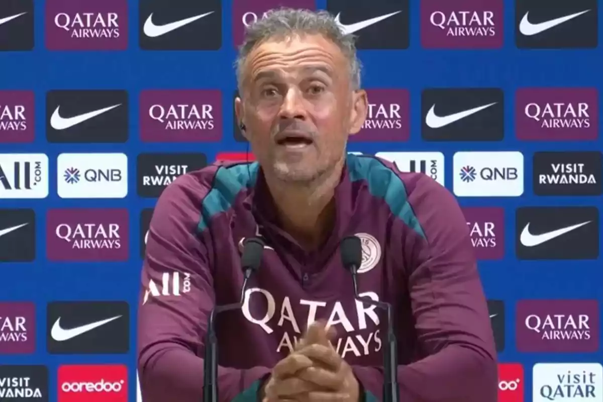 A man at a press conference with a background of sports sponsor logos.