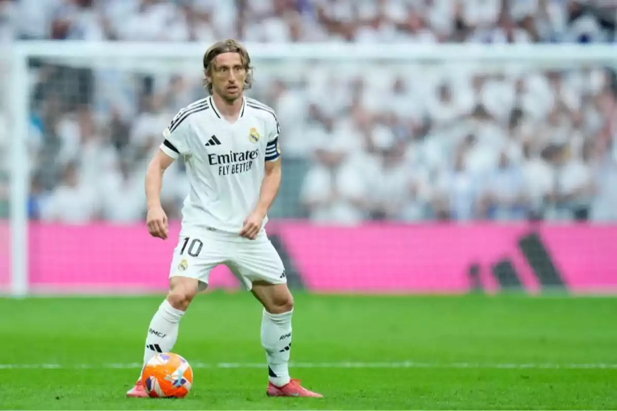 Futbolista con uniforme blanco del Real Madrid controlando el balón en un estadio lleno de aficionados Futbolista con uniforme blanco del Real Madrid controlando el balón en un estadio lleno de aficionados